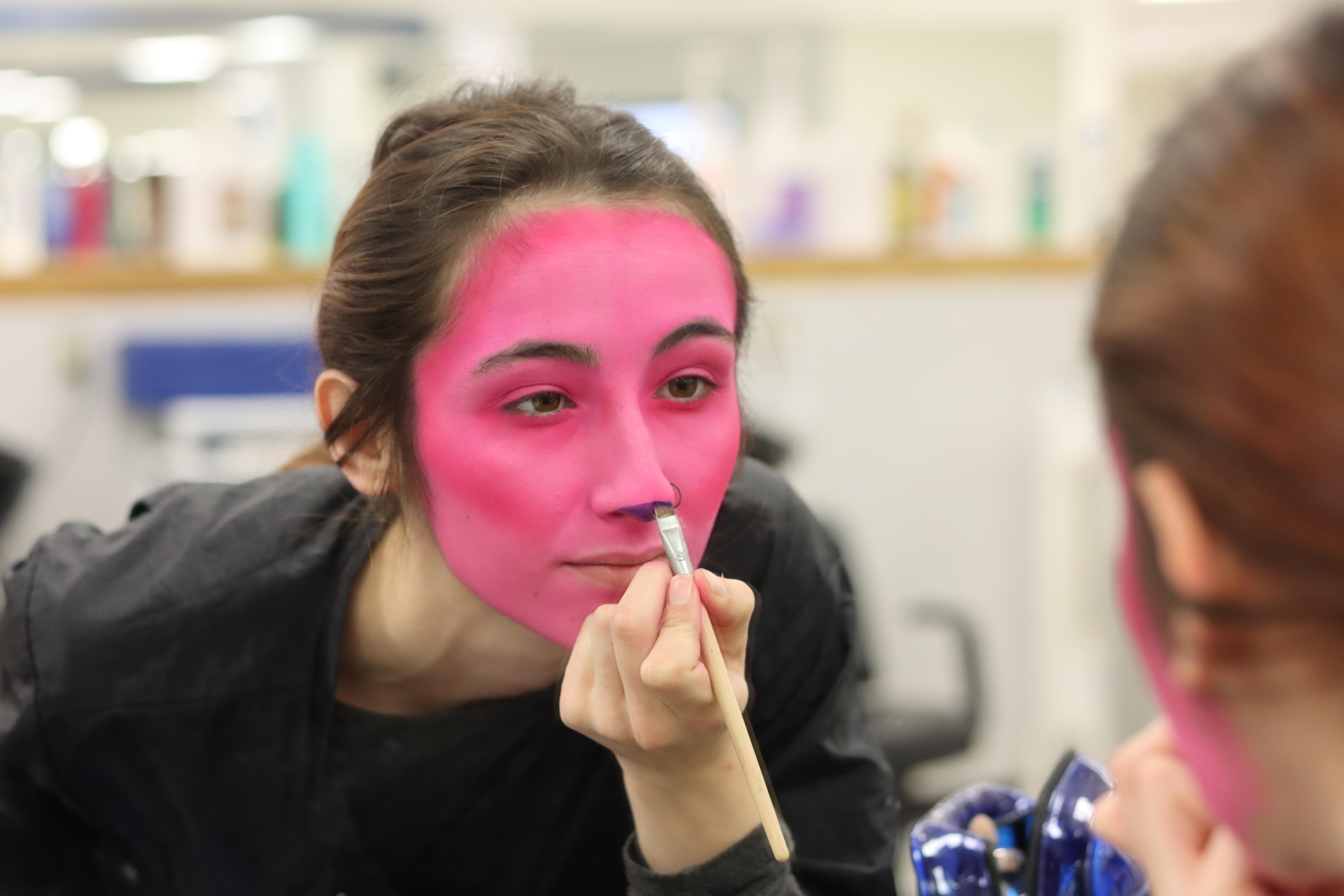 Cosmetology student putting hot pink halloween makeup on their face